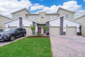 A modern two-story house with a driveway, a parked car, and a red door. - Cozy 3BR/2BA Condo in ChampionsGate, Near Disney (Kissimmee)