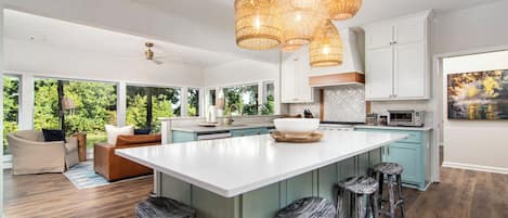 Een moderne keuken met een groot schiereiland, barstoelen, hanglampen en uitzicht op de omgeving.