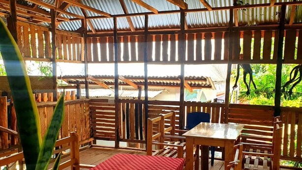 Un espace extérieur aménagé avec des meubles en bois et une table, protégé par un toit en tôle ondulée.