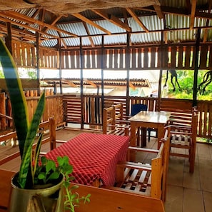 A covered outdoor seating area with wooden furniture and a table, surrounded by a corrugated metal roof. - CAVEJESUS PARK LODGE (Himo)