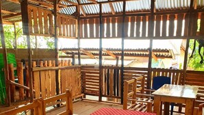 Une terrasse extérieure en bois, avec une nappe à carreaux rouges, des chaises en bois et un toit en tôle ondulée.