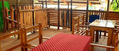 An outdoor wooden deck with a red checkered tablecloth, wooden chairs, and a corrugated metal roof.