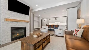 Ein modernes Wohnzimmer mit Kamin, einem Holztisch, einem braunen Ledersofa und einem Essbereich im Hintergrund.