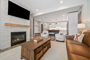 Ein modernes Wohnzimmer mit Kamin, einem Holztisch, einem braunen Ledersofa und einem Essbereich im Hintergrund.