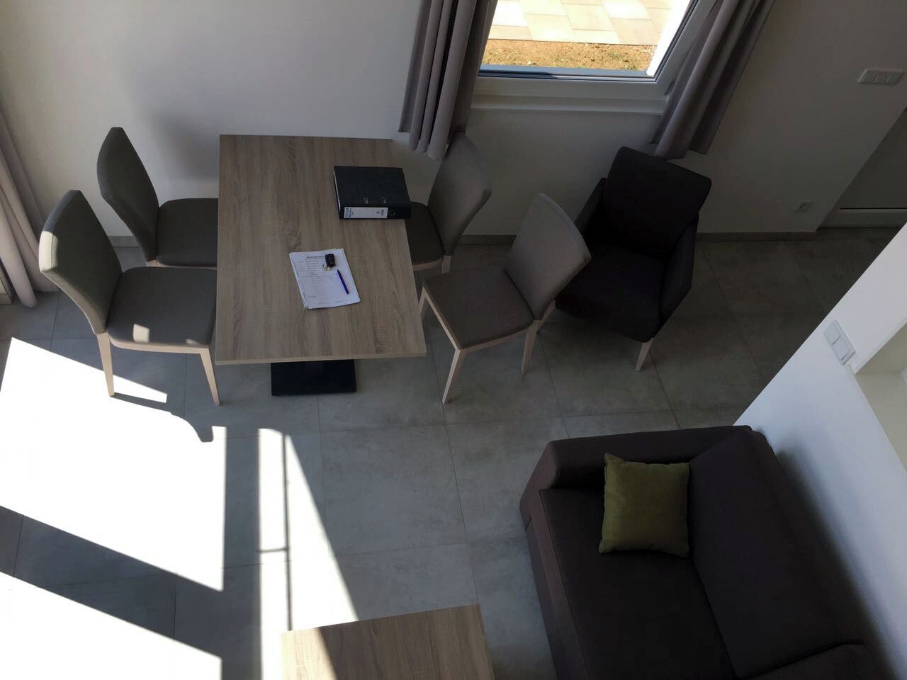 Ett modernt rum med ett träbord, fyra stolar, en mörk soffa och ett fönster med gardiner.