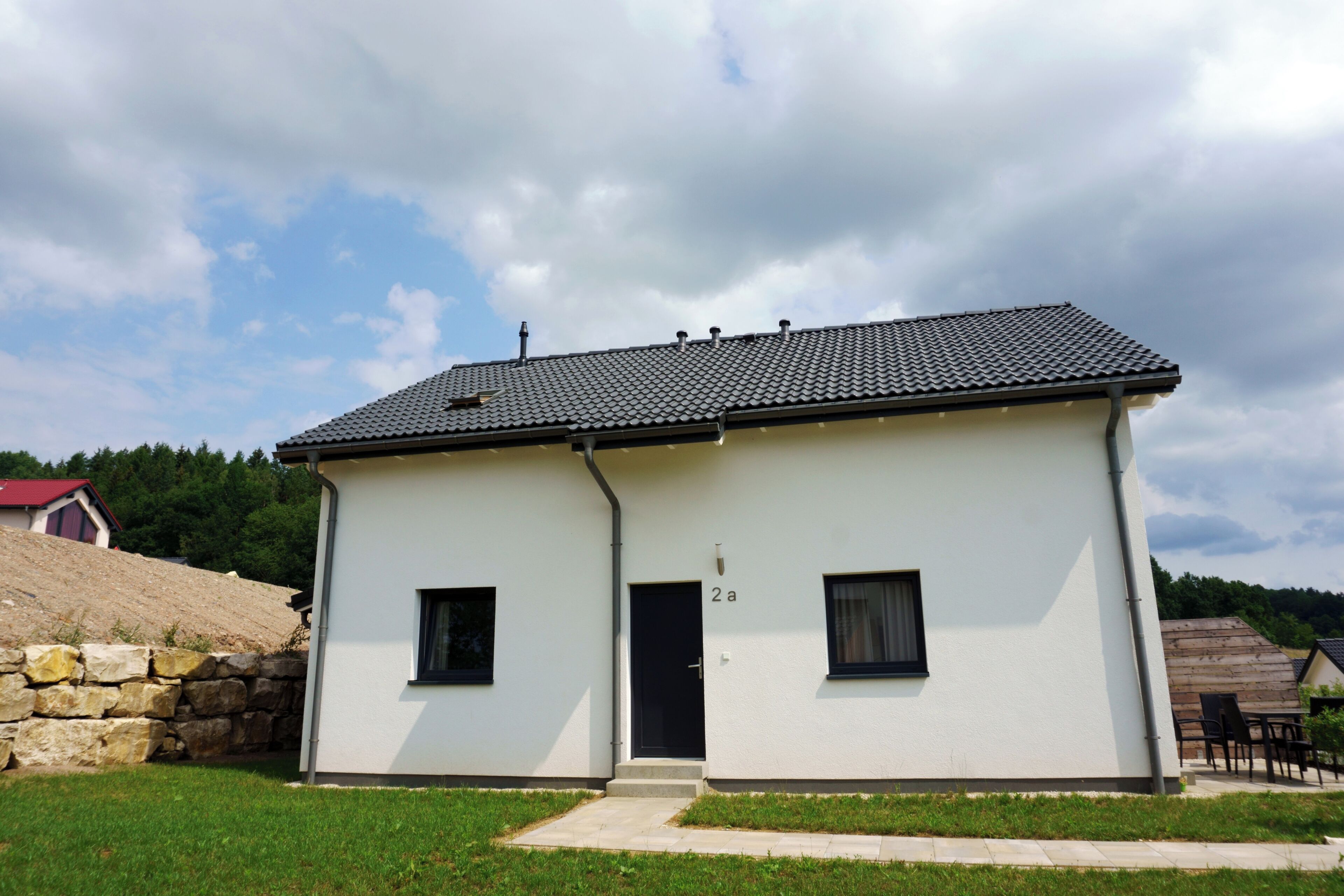 A two-story building with a tiled roof, a stone wall, and a grassy yard.
