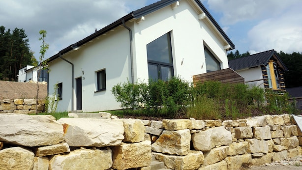 Ein modernes Haus mit zwei Etagen, einer Steinwand, großen Fenstern und einem geneigten Dach.