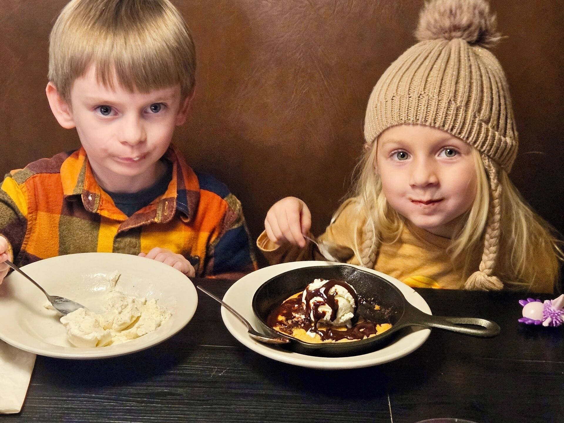 Twee kinderen zitten aan een tafel met borden eten.
