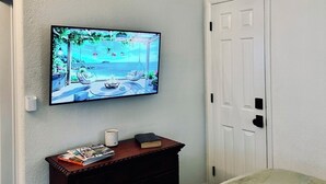 A bedroom with a bed, a television mounted on the wall, a wooden dresser, a white door, and a cabinet above the door. - Lone Oak Cottage Fully restored cabin with 5 beds & walk in shower (Medicine Park)