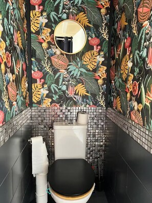 Une salle de bain avec des toilettes, un rouleau de papier toilette et un miroir au mur.