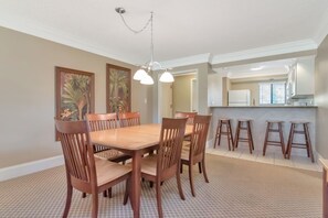 A dining area with a wooden table and chairs, a kitchen in the background, and a patterned floor.