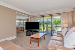 A hotel room with a large flat-screen TV, a sofa, a wooden coffee table, and a balcony with outdoor furniture. - Quiet Comfortable 2br-2ba Condo in Saddlebrook (Zephyrhills)