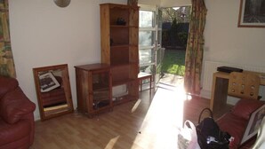 A living room with a red sofa, a wooden cabinet, a framed picture, and a window with curtains. - A good flat close to university! (Manchester)