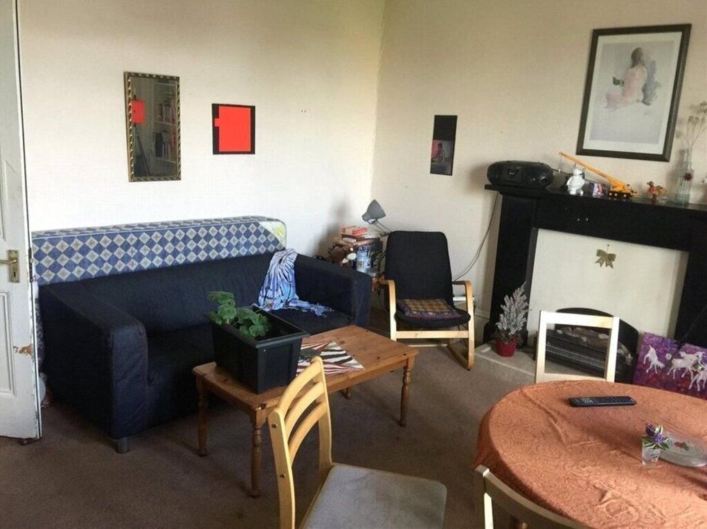 A living room with a sofa, a coffee table, a chair, a fireplace, and a small table with a remote control.