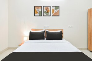 A hotel room with a bed, two pillows, a nightstand with a lamp, and three framed artworks on the wall. - Deluxe Aarian Tej Nilayam (Hyderabad)