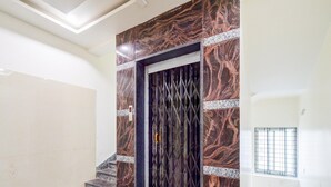 A staircase leading to a dark, patterned door with a metal gate, a small window with bars, and a light fixture on the ceiling. - Deluxe Aarian Tej Nilayam (Hyderabad)