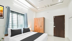 A hotel room with a bed, a wardrobe, a door, and a window with curtains. - Deluxe Aarian Tej Nilayam (Hyderabad)