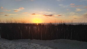 Ein Strand mit Sand und einem Zaun im Vordergrund, sowie ein Sonnenuntergang im Hintergrund.