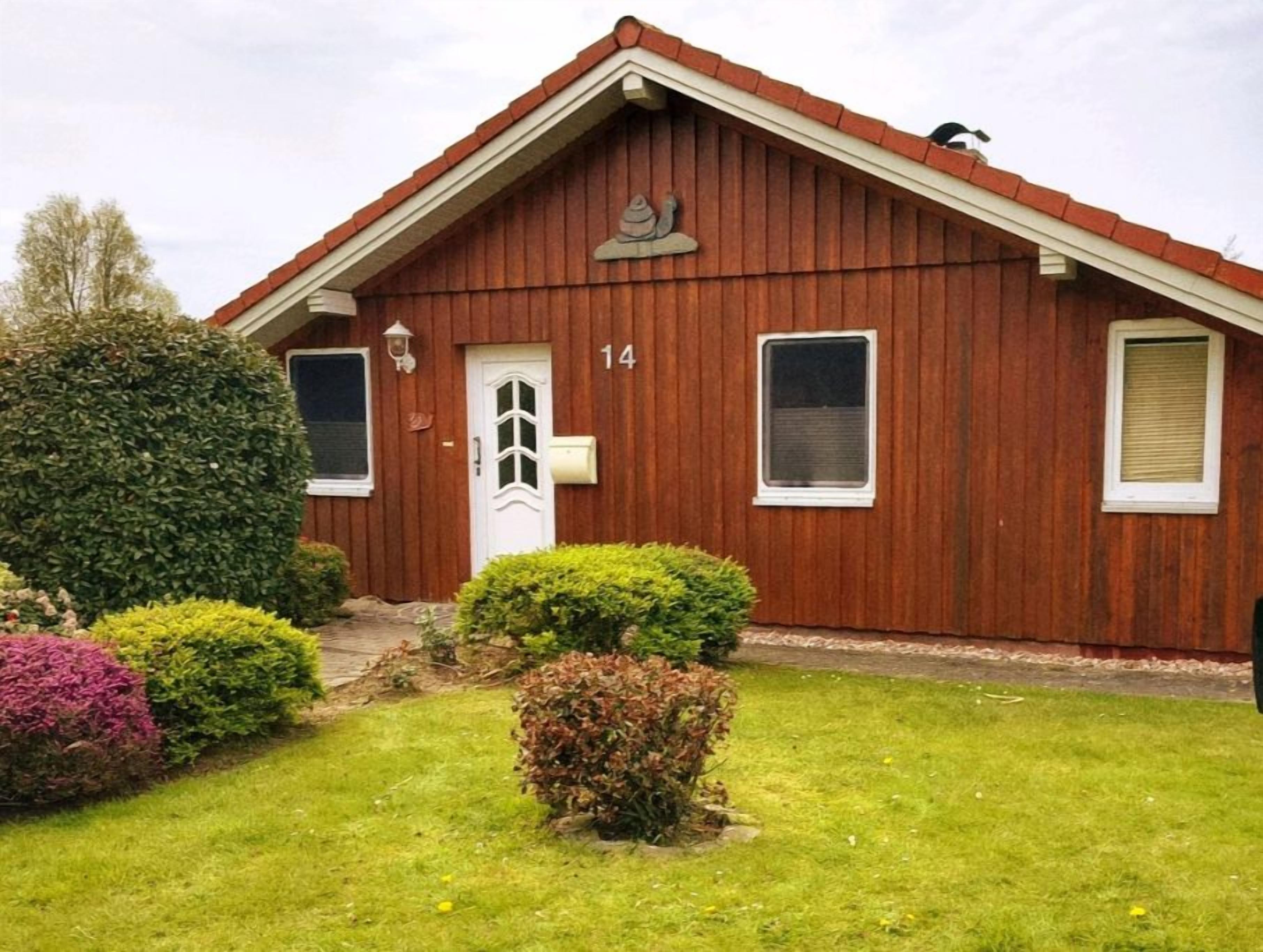 En röd träbyggnad med ett sadeltak, siffran ’14’ på framsidan och en liten veranda med en dörr.