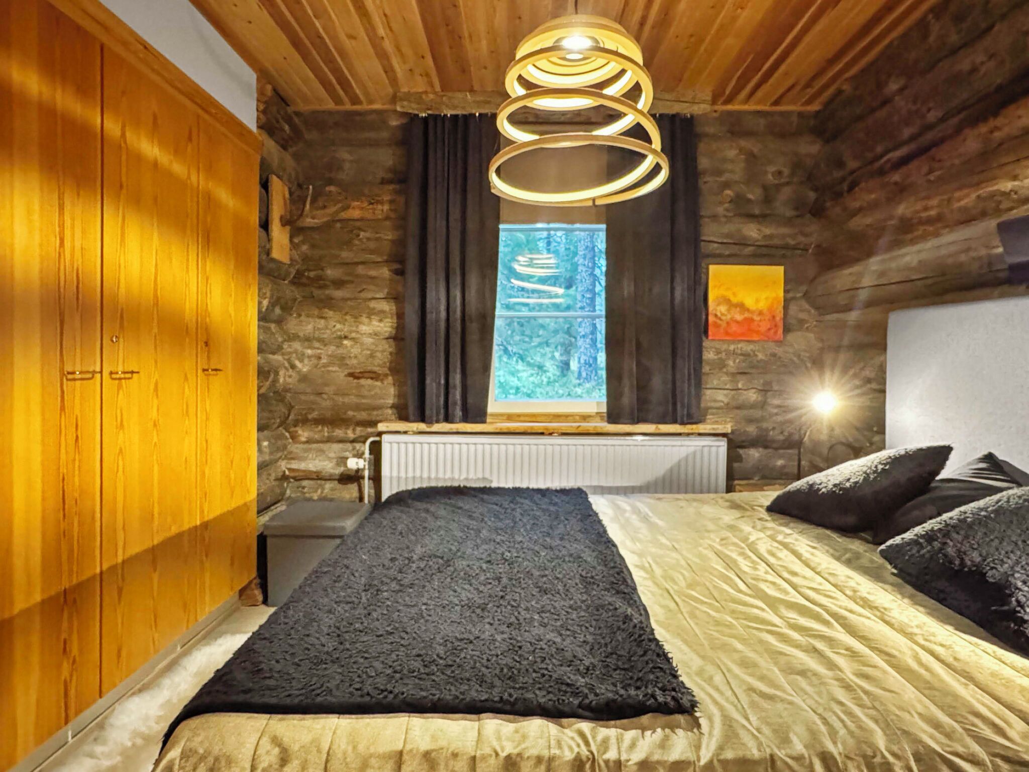 Una camera da letto con un letto, una finestra con tende, un termosifone, pareti in legno e una lampada a soffitto.