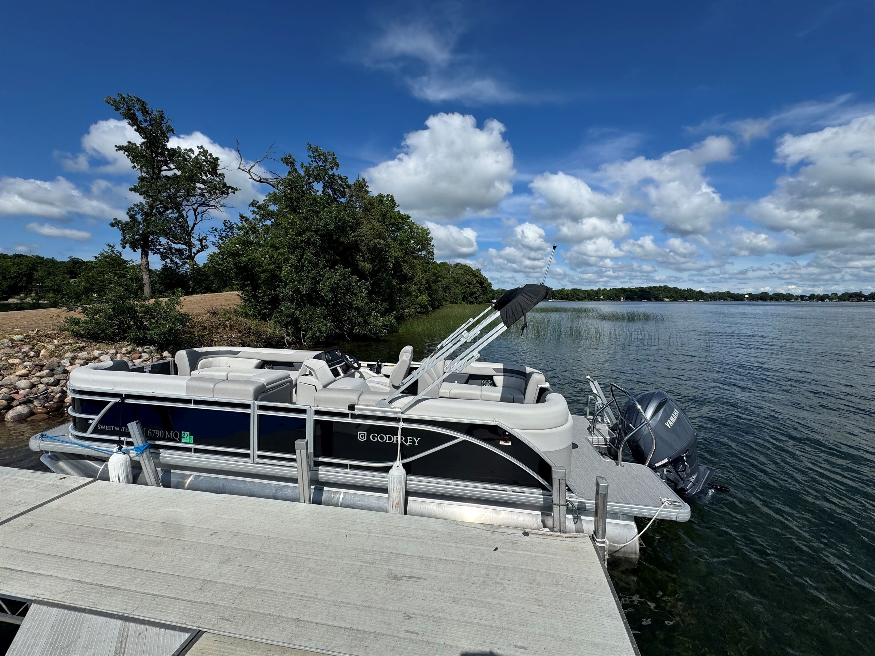A boat docked at a pier with a Yamaha outboard motor, a steering wheel, and a brand name 'GODFREY' on the side.
