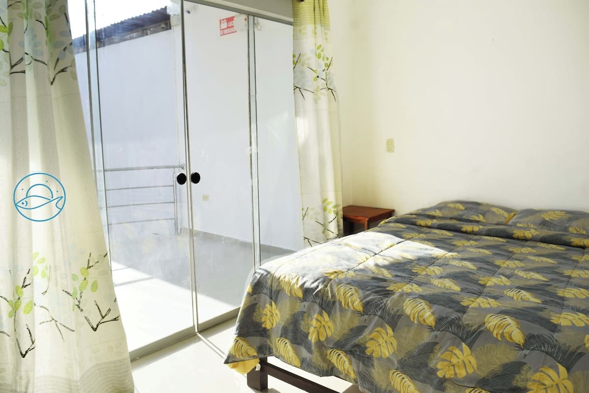 A room with a bed, a small table, a sliding door, and a view of the outside.