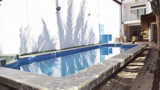 Una piscina con bordatura piastrellata, un edificio bianco sullo sfondo e un vialetto in pietra.