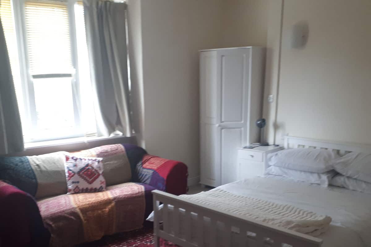 A bedroom with a bed, a small bedside table, a wardrobe, a window with curtains, and a patterned carpet.