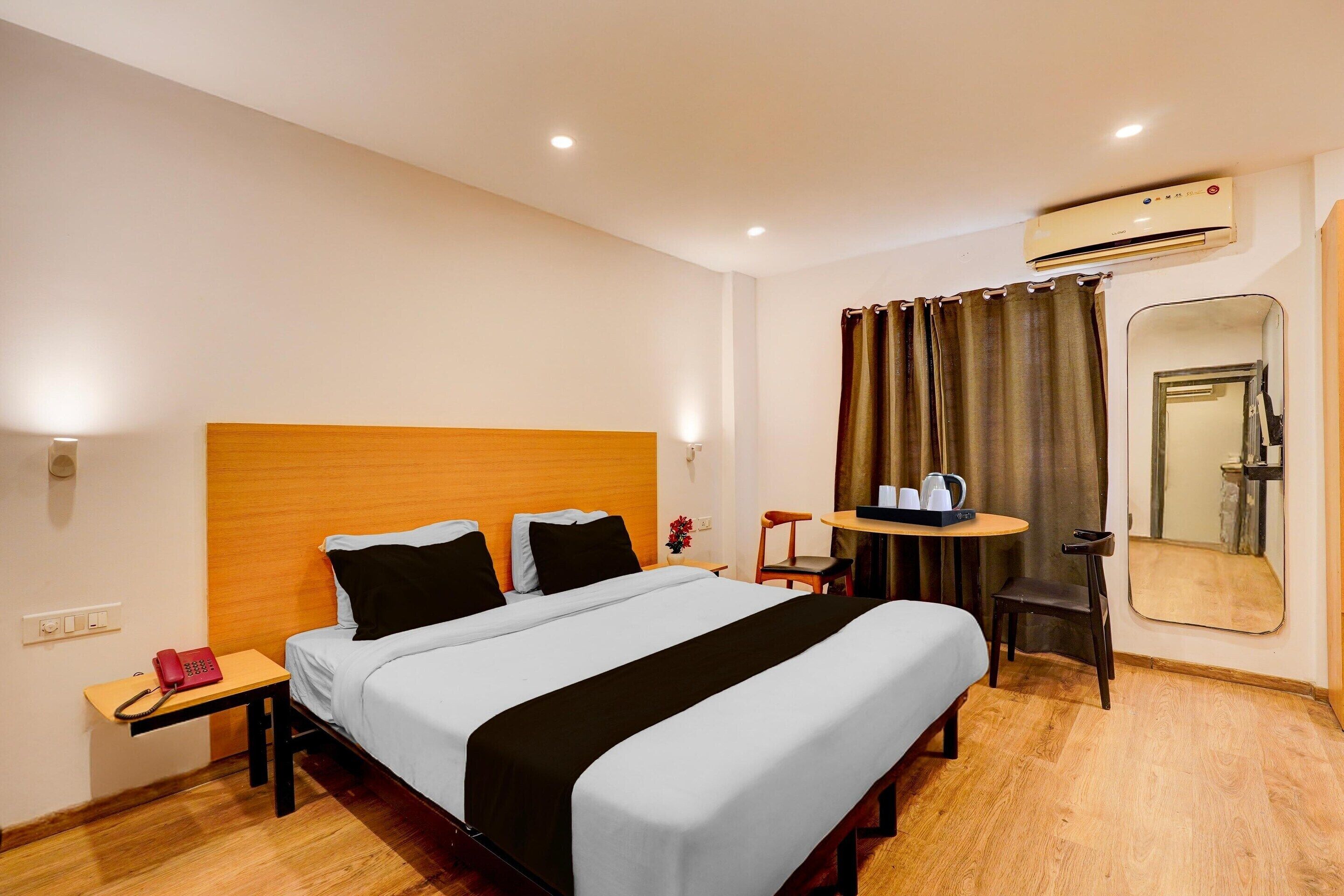 Habitación de hotel con cama, mesita de noche, silla, una pequeña mesa y equipo de aire acondicionado.