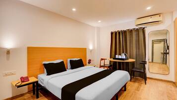 Habitación de hotel con cama, mesita de noche, silla, una pequeña mesa y equipo de aire acondicionado.