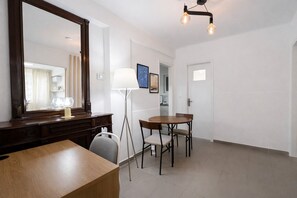 A hotel room with a wooden desk, a large mirror, a floor lamp, a dining table with chairs, and a modern ceiling light fixture. - Stylish Lower Ground Apt in Vibrant Kypseli by ΜΡS (Athina)