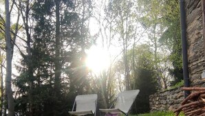 A grassy outdoor area with two white chairs, a stone wall, and trees. - Baita Carlito - Quiet and sunny setting overlooking the forest (Sueglio)