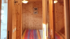 A wooden cabin interior with a bed, wooden walls, and a ceiling light. - Baita Carlito - Quiet and sunny setting overlooking the forest (Sueglio)