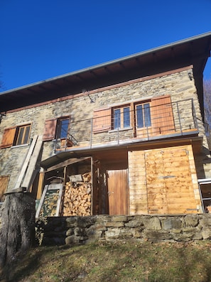 Un edificio de piedra con contraventanas de madera, una escalera y una pila de leña.