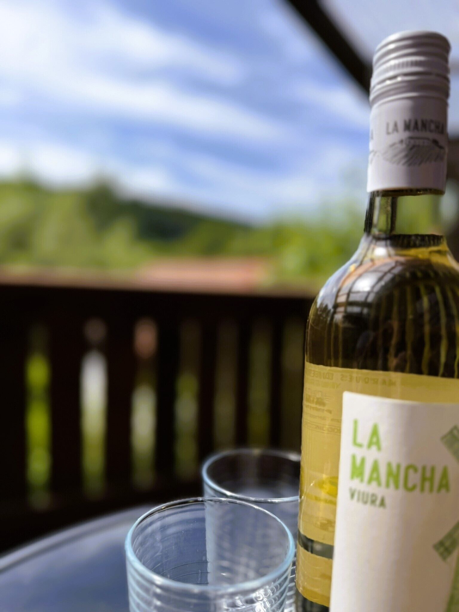 Une bouteille de vin de La Manche, avec son étiquette, est posée sur une table à côté de deux verres vides.