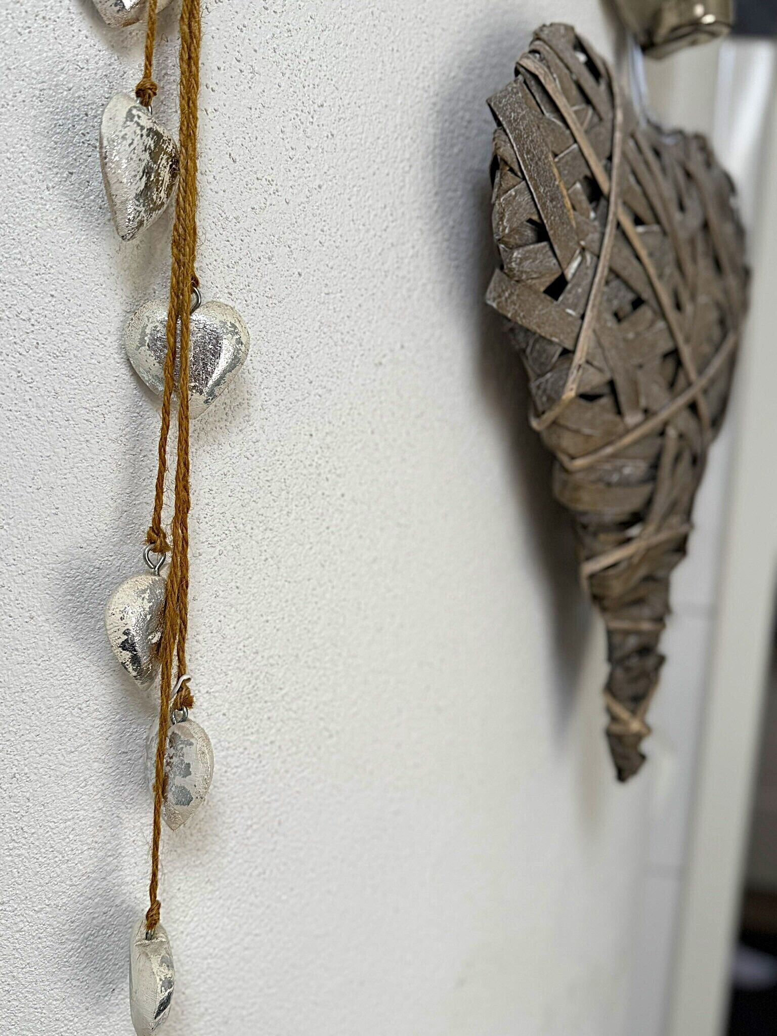 Pared com superfície texturizada e um objeto decorativo composto por um cordão de contas e um objeto tecido.