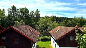 Two wooden cabins with red roofs, a grassy yard, and a forested hill in the background. - Peaceful COZY Apartment in Bavarian Forest +WIFI (Grafenwiesen)