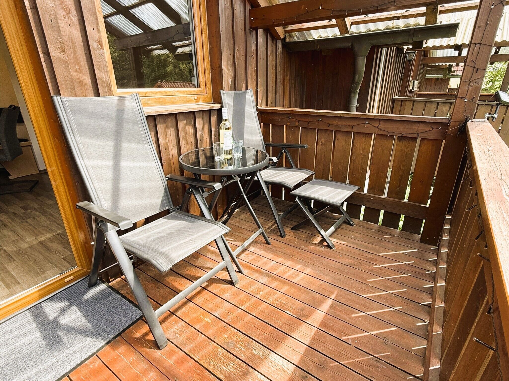 Une terrasse en bois avec une table en verre et deux chaises.