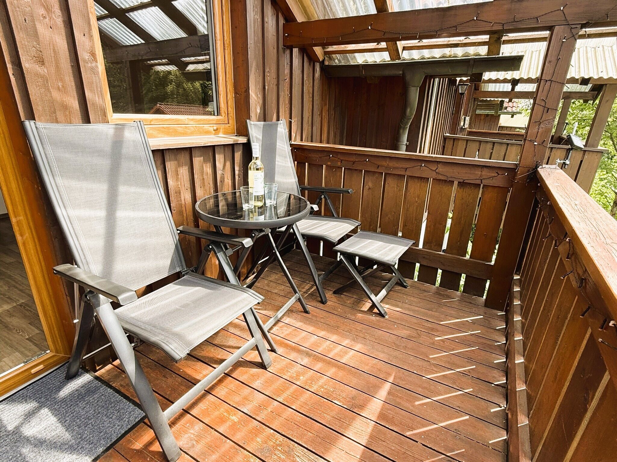 Eine Holzterrasse mit einem Glastisch und Metallstühlen.