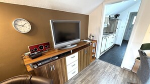 A modern living room with a flat-screen TV, wooden cabinets, a leather sofa, and a kitchen in the background. - Peaceful COZY Apartment in Bavarian Forest +WIFI (Grafenwiesen)