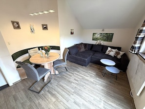 A modern living space with a round dining table, two grey armchairs, a dark sectional sofa, and a small white table. - Peaceful COZY Apartment in Bavarian Forest +WIFI (Grafenwiesen)
