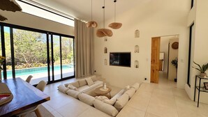 Ein modernes Wohnzimmer mit großem Fenster, einer Eckcouch, einem Esstisch und einem an der Wand befestigten Fernseher.