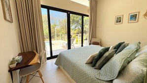 Ein Schlafzimmer mit Bett, Schreibtisch und Blick auf einen Balkon mit Gartenmöbeln.