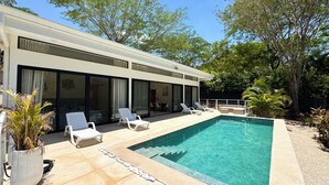 Ein modernes Haus mit Swimmingpool, Sitzgelegenheit im Freien und großen Fenstern.