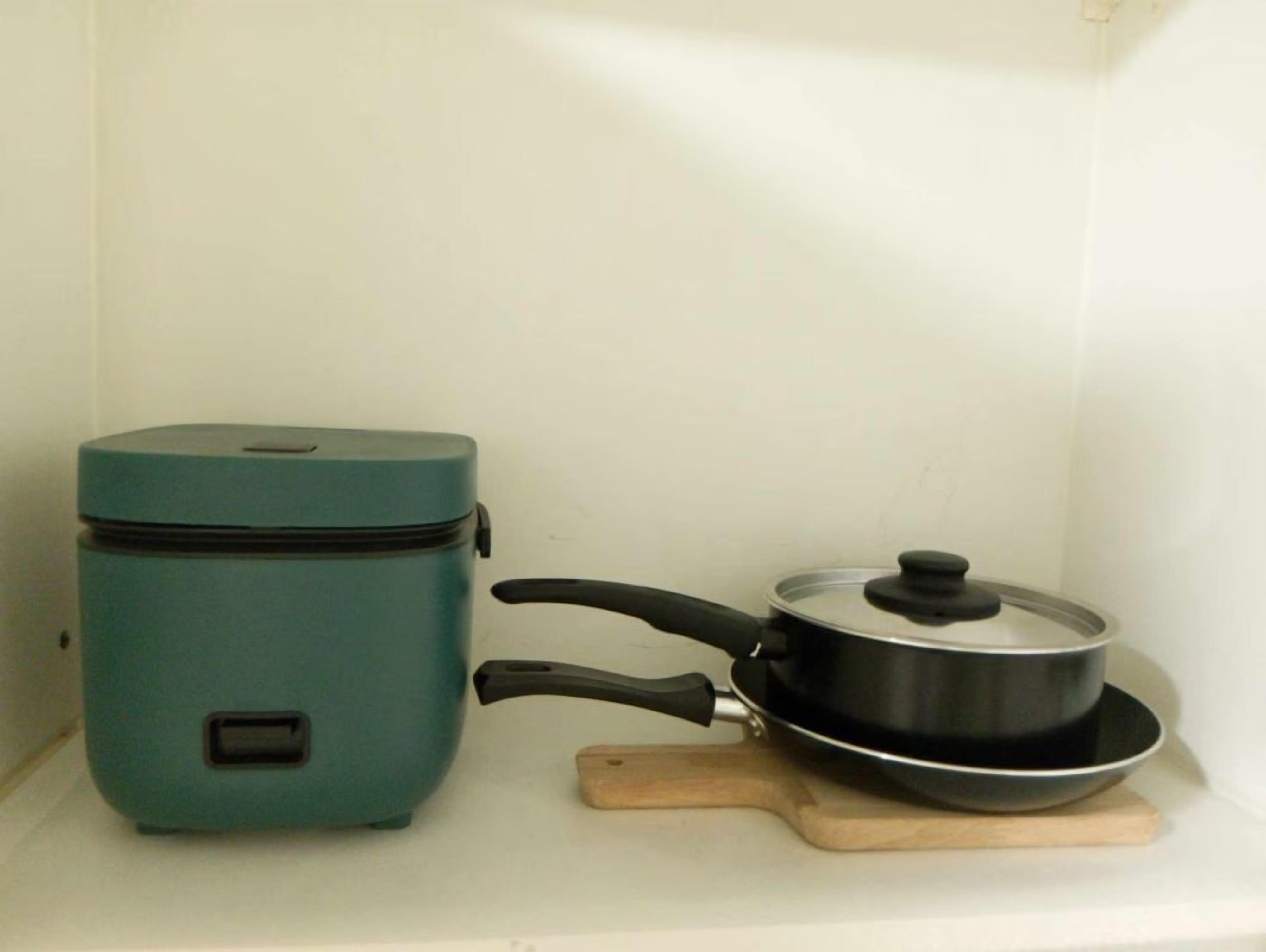 A compact teal appliance, possibly a rice cooker, and a black pot with a lid on a wooden cutting board.