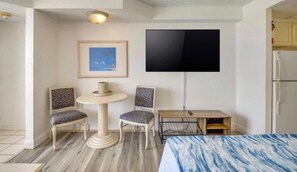 Habitació d'hotel amb un llit, dues cadires, una taula petita, un televisor i un quadre al mur.