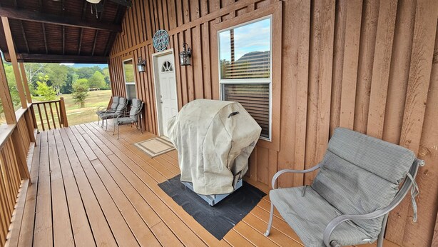 Eine Holzterrasse mit überdachter Grillgelegenheit, einem überdachten Tisch und einem Stuhl.