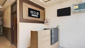 Ein Hotelrezeptionstresen mit einem 'HOTELO'-Schild, einem montierten Fernseher und einer Überwachungskamera.