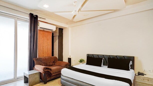 Ein modernes Hotelzimmer mit einem großen Bett, einem Ledersessel, einem kleinen Tisch und einer Schiebeglasdoor zum Balkon.