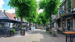 Eine Kopfsteinpflasterstraße gesäumt von Außenbestuhlung, Bäumen und Gebäuden mit sichtbarer Beschilderung.